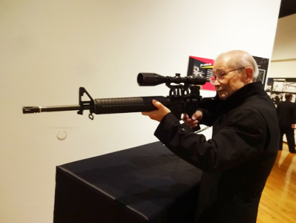 ゴルゴの愛用銃Ｍ16アーマライトを構える土岐さん＝2018年ゴルゴ展（川崎市市民ミュージアム）