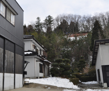 土砂災害発生箇所の西側。裏山の上部の赤土が見える付近で建設業者が樹木を伐採し、浸水防止のブルーシートを掛ける準備を進めていた。手前は避難世帯の住宅など＝7日午前10時ごろ、鶴岡市西目字斎藤