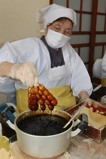 団子にたっぷりと黒蜜を付ける菅原タミ子さん