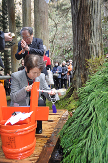 参拝者たちが龍王沢の清水をひしゃくで受け、朱色のたるに注いだ