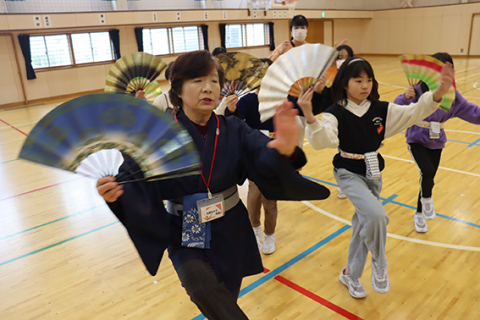 メンバーの佐藤たみ子さんから扇子のさばき方や足の運び方を教わる子どもたち