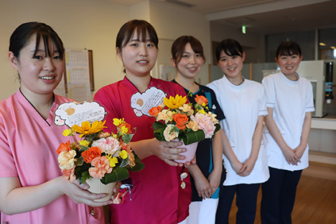 「患者さんや家族の見えやすい場所に飾ります」と看護学生（右側の白衣）から贈られた花かごを持つ荘内病院のナース