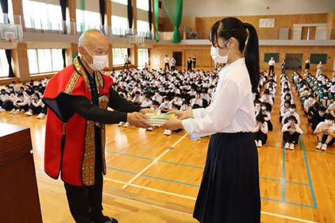 全校生徒の前で生徒代表の渡部さんに本を寄贈する松尾さん（左）＝10日、鶴岡二中