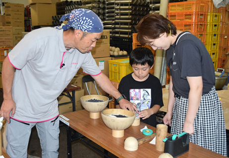 安藤孝二さん（左）の指導を受けながら花火製作を体験する家族連れ