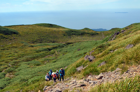 岩場が続く登山道。後ろには日本海に浮かぶ飛島が見える