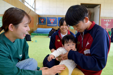 抱き方を教わりながら赤ちゃんを抱っこする生徒たち