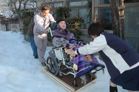 車いすのお年寄りをソリに乗せて移送する職員