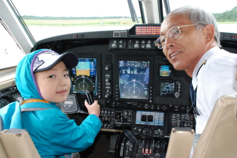 高谷機長（右）の指導で操縦かんを握りご満悦の男の子＝2日午前11時41分、庄内空港エプロン