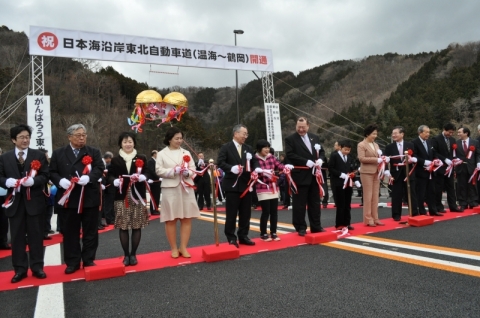 関係者がテープカットを行い、日沿道のあつみ温泉ＩＣ―鶴岡ＪＣＴ間の開通を祝った＝24日、鶴岡市大岩川・あつみ温泉ＩＣ本線