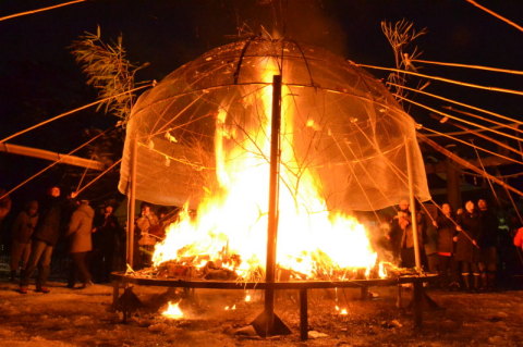 縁起物が浄火でたき上げられる中、参拝客が「おさがり」のスルメなどを竹棒であぶった