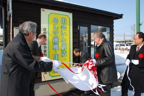 町営バス停待合所に設置された庄総高支援看板の除幕式が行われた＝ＪＲ余目駅前