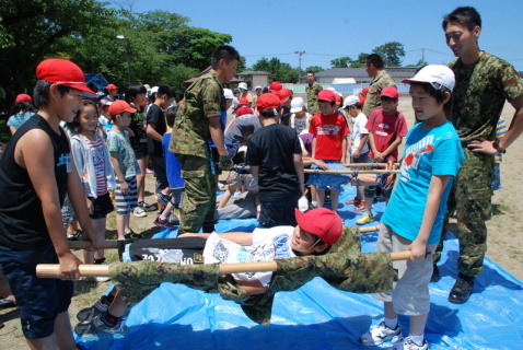 自衛隊員が作った簡易担架を使い搬送訓練に挑む浜田小の児童たち