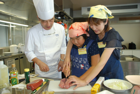 阿部シェフ（左）の指導で協力しながらステーキ肉の切り分けに取り組む親子