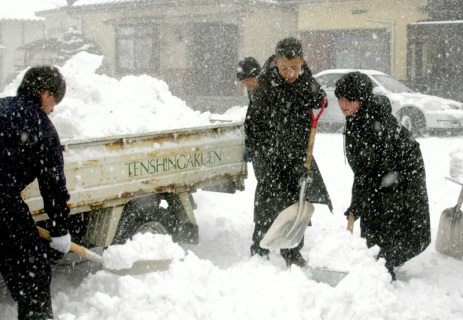 吹雪の中、民家前で除雪作業を行う天真学園高の生徒たち