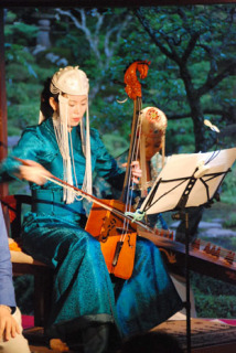 玉川寺の庭園を背景に馬頭琴を演奏するイラナさん