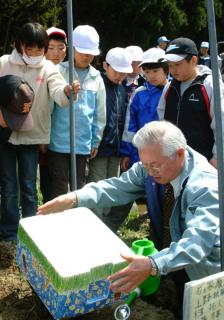 工藤会長（手前）の指導でホタルの幼虫を放流する児童たち