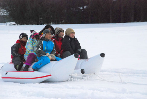 雪原をバナナボートで疾走する鹿児島と松山地域の子どもたち＝21日、地見興屋小近く