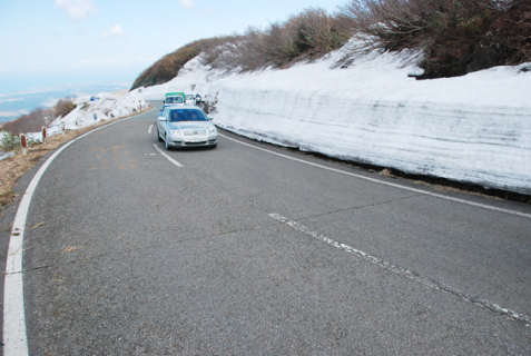 青空の下、雪の壁を横目にパレードの車が県境を目指した