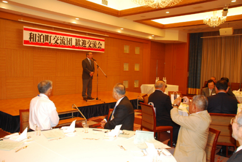 酒田市での歓迎交流会で、和泊町の前田副町長（壇上）が一層の交流を呼び掛けた＝24日夕