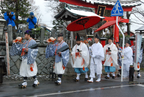 朝方は小雪が舞う中、「松例祭」の浄財集めとなる松の勧進がスタート。松聖が小聖の山伏を従えて商店街などを回った＝1日午前