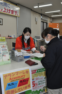 郵便局員がオレンジ色の公式Ｔシャツ姿で、来局した市民に応対した＝8日、鶴岡本町二郵便局