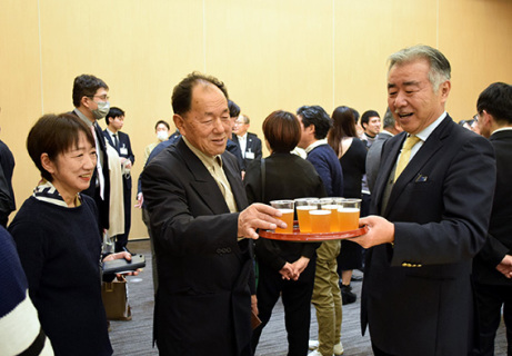 お披露目会で参加者にビールを勧める池田社長（右）