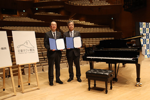 荘銀タクト鶴岡の命名権更新に署名した松田頭取（右）と皆川市長。右側は演奏体験ができるスタインウェイ社製のグランドピアノ