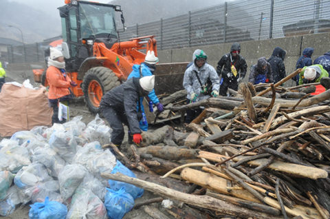 強い風雪が吹き付ける中、学生たちが漂着ごみや流木を回収した＝13日、鶴岡市の油戸海岸