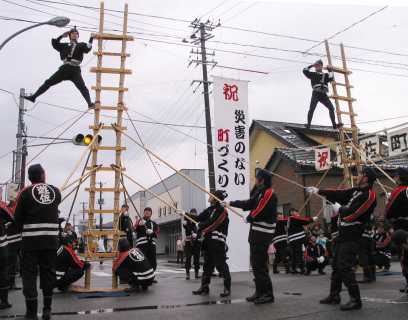 はしご乗りの演技とともに無災害を祈る垂れ幕が掲げられた＝荘内銀行遊佐支店前