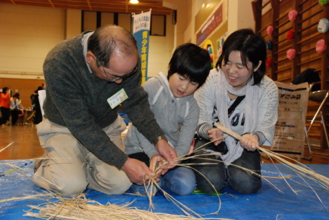 青少年育成推進員（左）の指導で縄ないに挑む親子連れ