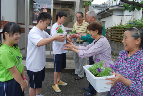 交流のある町内会などへ種から育てた花のプランターを届けた養護学校の生徒たち＝19日、大塚町公民館