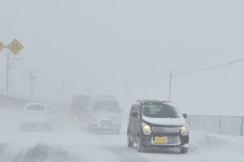 幹線道路は断続的な地吹雪となり、車両はライトを点灯しスピードを落として走行＝25日午前９時半ごろ、鶴岡市文下