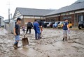 氾濫した荒瀬川から敷地内に流れ込んだ泥をかき出す地区住民たち＝27日午前、八幡保育園前